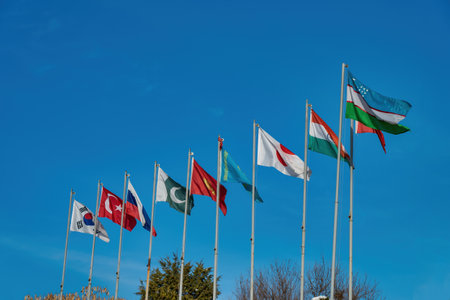 Flags of uzbekistan, japan, south korea, turkmenistan, kyrgyzstan, kazakhstan, turkish and russian waving against the blue sky.の写真素材