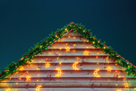 Christmas balls, toys and glowing garlands on an artificial spruce branch and wooden house background.の写真素材