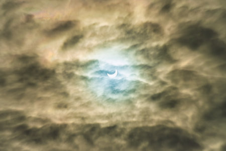 Partial solar eclipse passing behind dramatic clouds.の写真素材