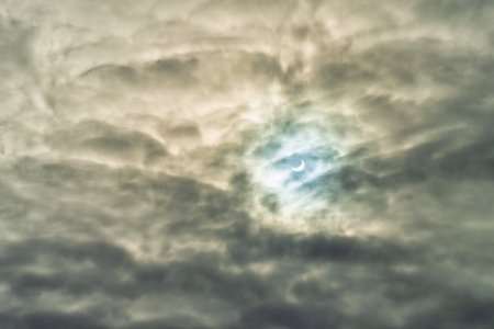 Partial solar eclipse passing behind dramatic clouds.の写真素材