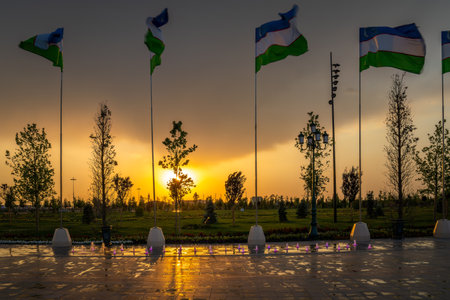 Flags of Uzbekistan waving on a sunset or sunrise dramatic cloudy sky background.