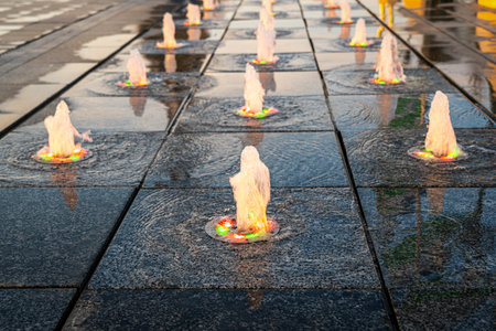 Small fountains on the sidewalk, illuminated by sunlight at sunset or sunrise in the park at summertime.の写真素材