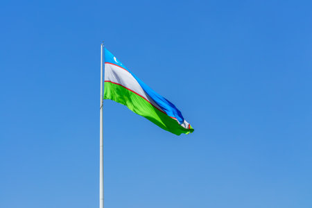 Flag of Uzbekistan waving on a daytime blue sky background.の写真素材