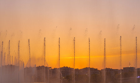 Big fountains on the artificial pond, illuminated by sunlight at sunset in Tashkent city park at summertime evening.の写真素材