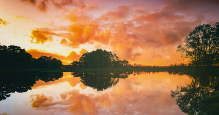 Sunrise or sunset on a lake or river with dramatic cloudy sky reflection in the water in summertime. Aesthetics of vintage film.の写真素材