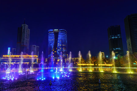 Uzbekistan, Tashkent - September 27, 2023: A fountain with laser illumination and light music in Tashkent City Park at nighttime against the backdrop of a scyscrapers.のeditorial素材