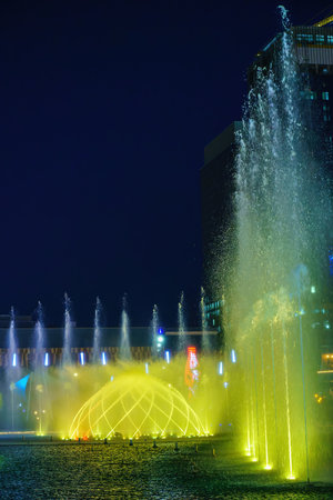 Uzbekistan, Tashkent - September 27, 2023: A fountain with laser illumination and light music in Tashkent City Park at nighttime against the backdrop of a scyscrapers.のeditorial素材