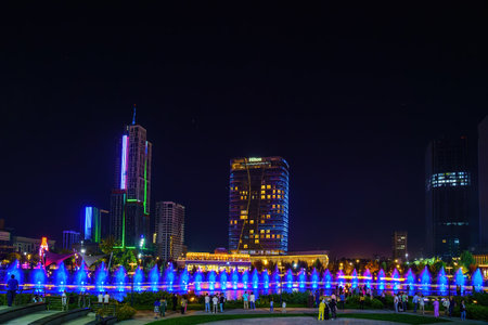 Uzbekistan, Tashkent - September 27, 2023: A fountain with laser illumination and light music in Tashkent City Park at nighttime against the backdrop of a scyscrapers and Hilton Hotel building.のeditorial素材