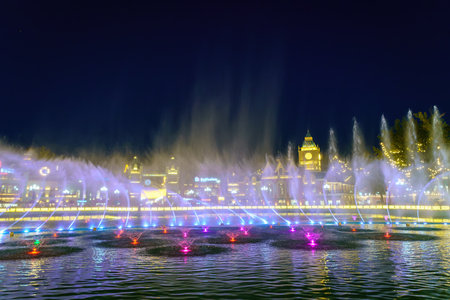 Uzbekistan, Tashkent - September 27, 2023: A fountain with laser illumination and light music in Magic City Park at nighttime against the backdrop of a decorations and buildings.のeditorial素材