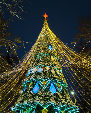Artificial Christmas tree in garlands at night park. Xmas decorations and lights.の写真素材