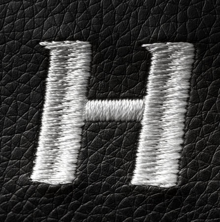 Letter H embroidered with white threads on black leather background. English alphabet. Element for design.の写真素材