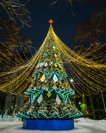 Artificial Christmas tree in garlands at night park. Xmas decorations and lights.の写真素材