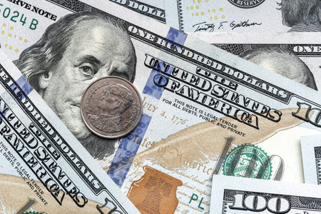 Close-up of a Thai Baht coin placed on US 100 dollar bills, on a white background. Concept of currency comparison and exchangeの写真素材