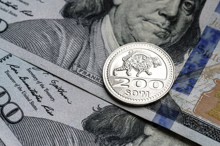 Close-up of a Uzbekistan som coin placed on US 100 dollar bills, on a white background. Concept of currency comparison and exchangeの写真素材