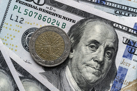 Close-up of a euro coin placed on US 100 dollar bills, on a white background. Concept of currency comparison and exchangeの写真素材