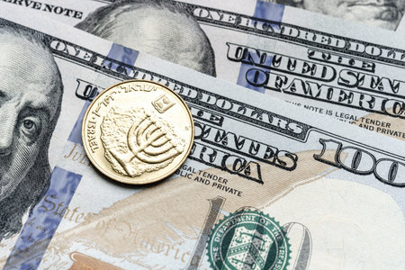 Close-up of a Israel shekel coin placed on US 100 dollar bills, on a white background. Concept of currency comparison and exchangeの写真素材