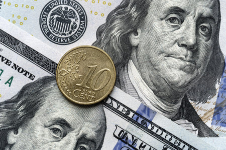 Close-up of a euro coin placed on US 100 dollar bills, on a white background. Concept of currency comparison and exchangeの写真素材