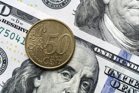 Close-up of a 50 euro cent coin placed on US 100 dollar bills, on a white background. Concept of currency comparison and exchangeの写真素材