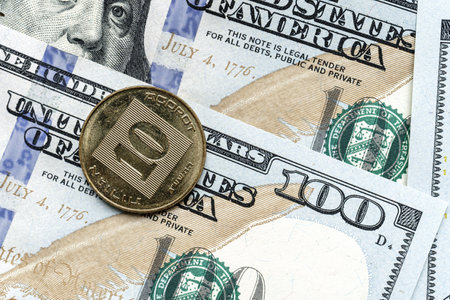 Close-up of a Israel shekel coin placed on US 100 dollar bills, on a white background. Concept of currency comparison and exchangeの写真素材