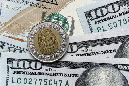 Close-up of a Egypt pound coin placed on US 100 dollar bills, on a white background. Concept of currency comparison and exchangeの写真素材