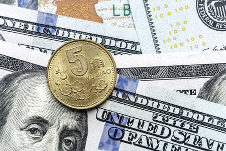 Close-up of a 5 Chinese wujiao coin placed on US 100 dollar bills, on a white background. Concept of currency comparison and exchangeの写真素材