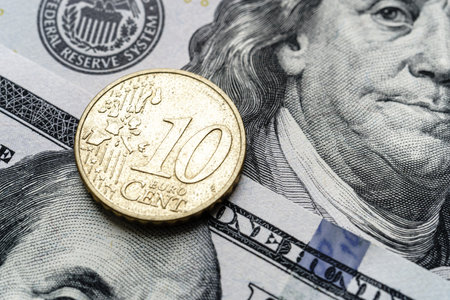 Close-up of a 10 euro cent coin placed on US 100 dollar bills, on a white background. Concept of currency comparison and exchangeの写真素材