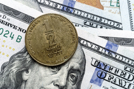 Close-up of a Israel shekel coin placed on US 100 dollar bills, on a white background. Concept of currency comparison and exchangeの写真素材