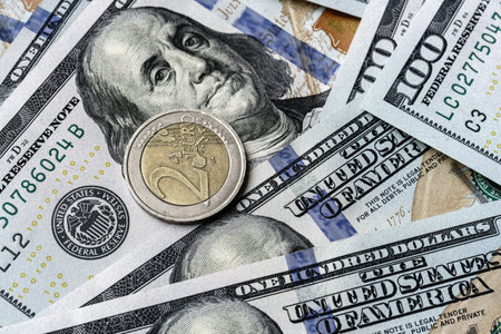 Close-up of a euro coin placed on US 100 dollar bills, on a white background. Concept of currency comparison and exchangeの写真素材