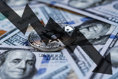Bitcoin coin on US hundred dollar bills and arrow down. Concept of falling e-commerce and cryptocurrency value in dollars.の写真素材