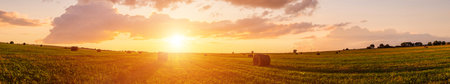 Scenic of sunset over hay bales in a field. Golden light bathes the landscape, creating a tranquil scene. For agriculture, travel and inspiring greeting card designs.の写真素材