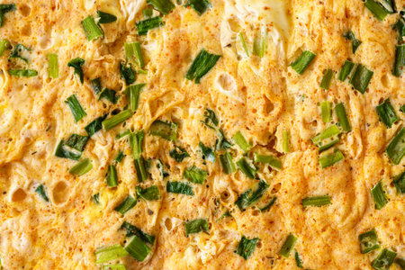 A macro shot capturing the texture of a homemade omelet cooked with fresh green onion slices....