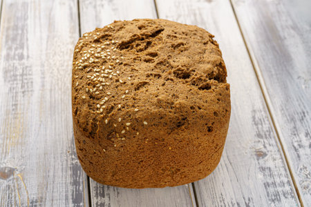 Whole grain bread loaf with sesame seeds and flax seeds on a rustic wooden table, healthy fresh...