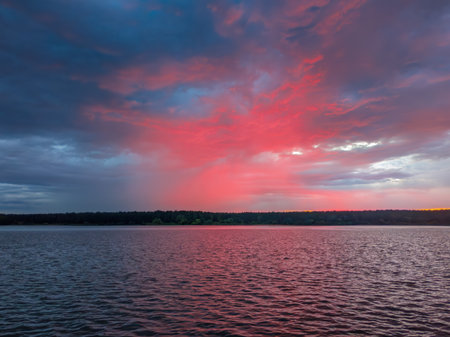 Red sky over a lake at dusk, creating a beautiful sunset or sunrise landscape for nature and travel concepts. Idyllic evening scene with calm water reflecting vibrant clouds.の写真素材