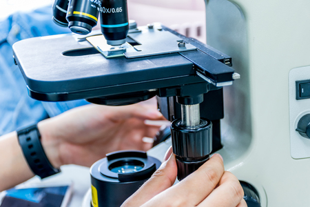 Close up view of scientist hands with a slide ofthe sample in the microscope for research in...