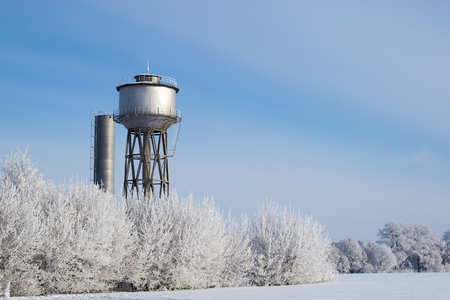 Small town water tower, lit by sunlight against a frozen landscapes.の写真素材
