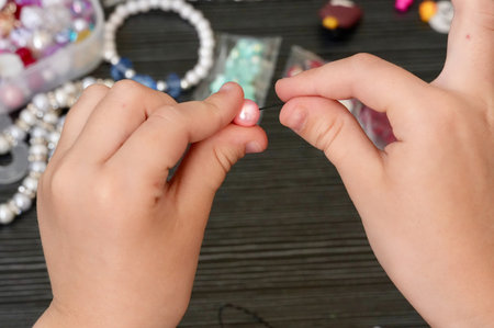 Hand of a child making a bracelet with beads on a wooden backgroundの写真素材