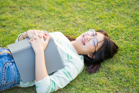 Asian Teenage girl  wearing eyeglasses lie on meadow with a book at sunsetの写真素材