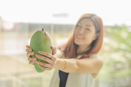 woman holding a fresh Mango in her hand and blur of womanの写真素材