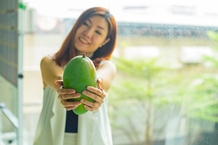 woman holding a fresh Mango in her hand and blur of womanの写真素材