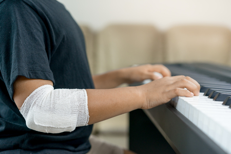 An asian boys at the wounded hands are playing the piano.の写真素材
