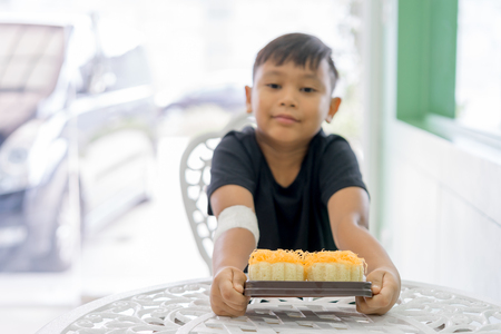 The boys at the wounded hands Hold a Gold Egg Yolk Thread Cakes in the hand on the table.の写真素材