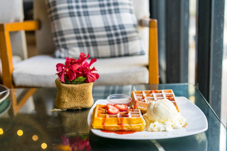Waffles with fresh ripe red strawberries and icecream served on a plate on table in the room of restaurantの写真素材