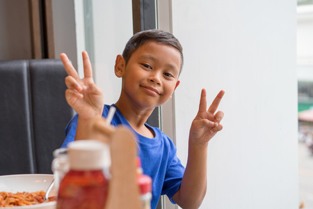 Cute asian boy seat at window eating food in a restaurant