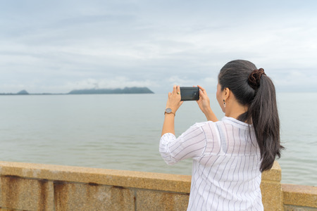 woman is standing taking photo with smartphone of  with fog on Khao Ta Mong Lai Forest Park background, Thailandの写真素材