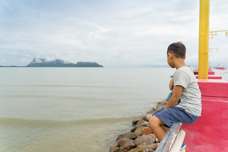Asian little kid sitting and looking at Saran-way Bridge Prachuap Khiri Khan Thailand  in day time.leisure and people conceptの写真素材