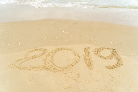 2019 written on sandy beach with wave approaching.