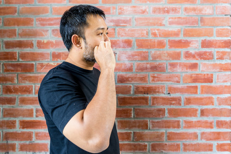 asian bearded man while smoking cigarette brick wall backgroundの写真素材