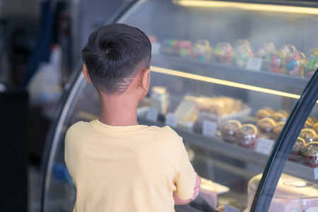 Asian kid boy waiting at bakery shop and choosing bakery that him likeの写真素材