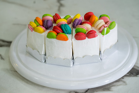 Cream cake decorated with macaron  on top, placed on a wooden plate