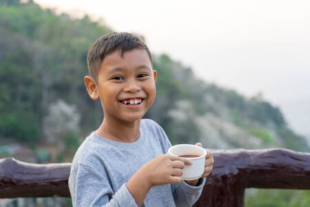 Asian kid boy is drinking water from the glass. With mountain views backgroundの写真素材